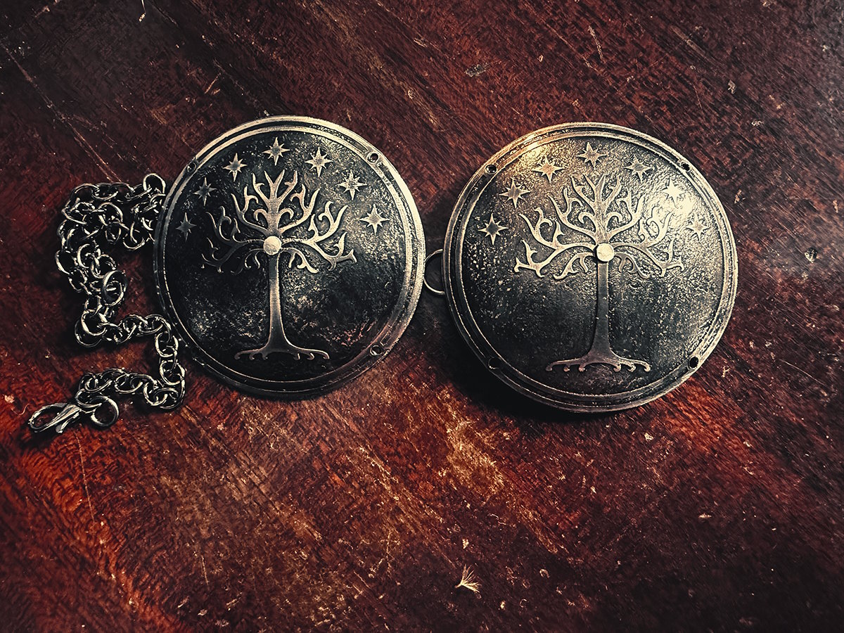 Photo of two shallow dome shaped steel discs with the tree of Gondor and seven stars etched into them, and a chain attached to one. They are about 2 inches in diameter.